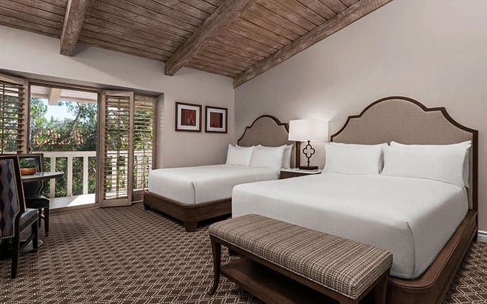 Outdoor patio with cushioned seating around a central fountain, overlooking a pool and landscaped gardens with trees and topiary.