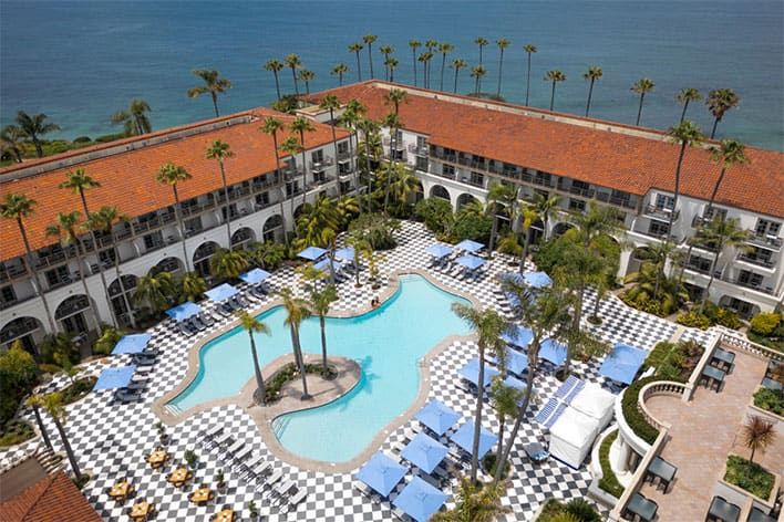 Aerial view of The Ritz-Carlton, Laguna Niguel with red-tiled roofs, a central outdoor pool, blue lounge chairs, and black-and-white checkered courtyard near the ocean.