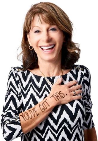 Speaker Sue smiling with her hand over her chest, displaying the words "YOU'VE GOT THIS." written on her forearm. She is wearing a black and white zigzag patterned top.