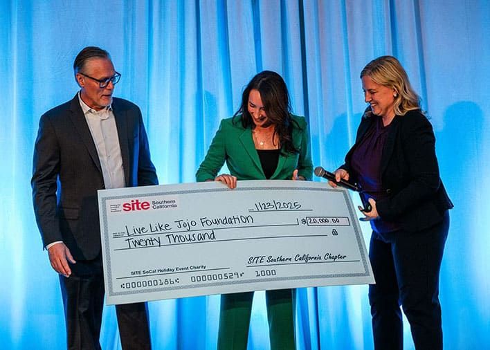 Three people stand on stage holding an oversized check for $20,000 made out to the Live Like Jojo Foundation from SITE Southern California Chapter.