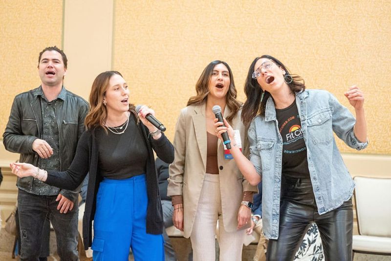 Four people singing enthusiastically into microphones at an indoor event.