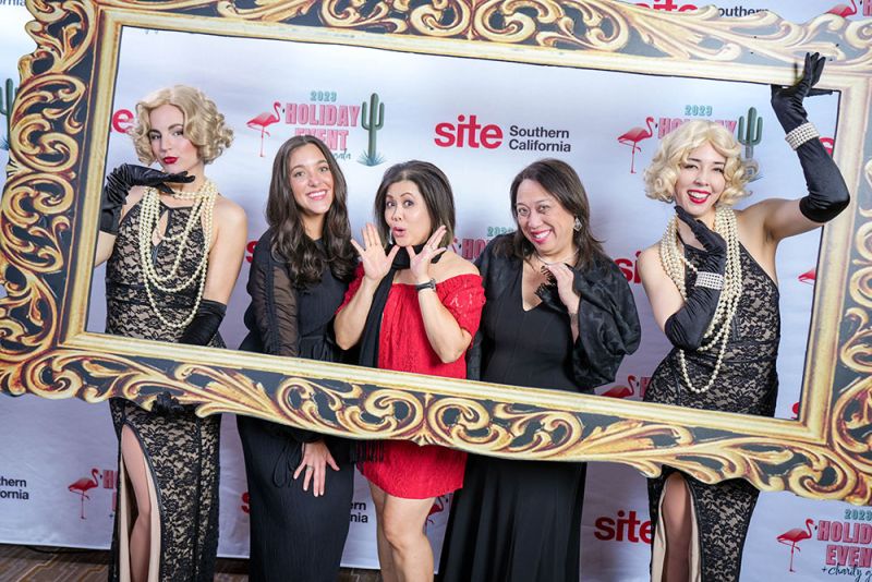 3 women posing with 2 models holding a large picture frame around them